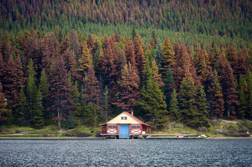 Boathouse with canoe on pier in autumn pine forest on hill in Maligne lake