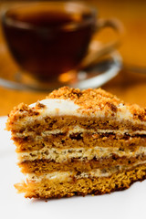 honey cake on a white plate on a wooden background with a cup of black tea in a glass cup