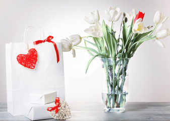 Shopping bag, red heart and ribbon, gift and white bouquet tulips bouquet in a vase on white background.