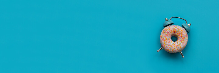 Banner 3:1. Pink alarm clock donut on blue background. Breakfast time or minimal concept. Copy space. Top view
