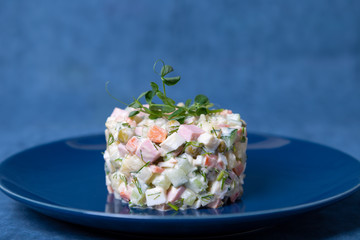 Olivier salad on a blue plate, decorated with pea sprouts. Traditional New Year and Christmas Russian salad. Close-up, selective focus, blue background.