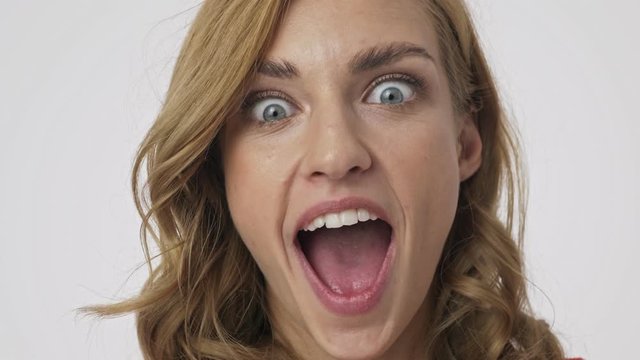Close up view of cheerful pretty blonde woman having fun and looking at the camera over grey background
