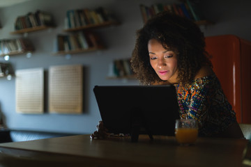 Afro hairstyle young woman working with digital tablet late at night or watching online media content in the dark.