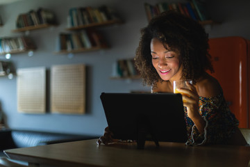 Afro hairstyle young woman working with digital tablet late at night or watching online media content in the dark.