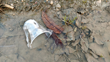 Used plastic cup discarded by side of the road in half frozen puddle, dirty and weathered. Plastic pollution concept. Waste plastic glass, closeup, selective focus, shallow depth of field.