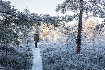 Woman standing in the middle of the woodland on the peat bog edge surrounded by the fresh snow and frost-clad winter landscape