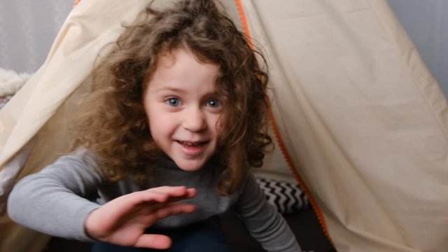 Little child vlogger saying hello hi looking at Camera at child room, cute kid talking to webcam making online recording having fun, curly girl with pretty face sitting in tent. slow motion