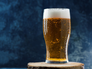 A glass of ice-cold light lager beer with water drops on dark background close-up