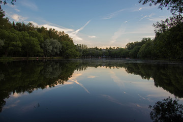 Yaroslavl. Warm evening in Neftyanik Park. Park refinery. Reflection of colorful sunset in the lake. Peace and quiet surrounded by green trees