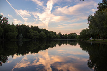 Yaroslavl. Warm evening in Neftyanik Park. Park refinery. Reflection of colorful sunset in the lake. Peace and quiet surrounded by green trees