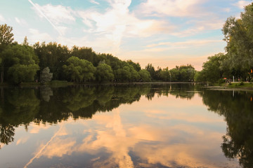 Fototapeta na wymiar Yaroslavl. Warm evening in Neftyanik Park. Park refinery. Reflection of colorful sunset in the lake. Peace and quiet surrounded by green trees
