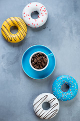 Espresso cup with coffee beans and different bright donuts over grey concrete background, vertical shot, above view