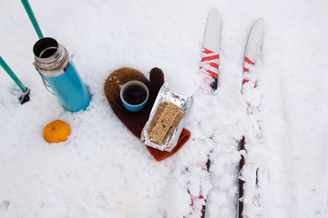 Flat lay of snow picnic while skiing with energy bar, coffee, mandarin, ski and mitten