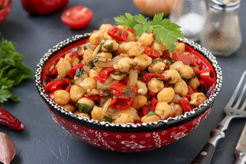 Garnish of chickpeas with pepper and tomatoes, a vegetarian dish rich in protein, located in a plate against a dark background horizontally