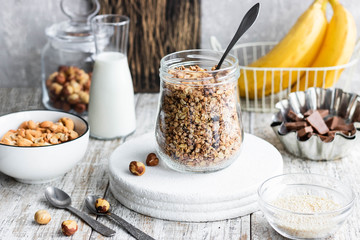 Chocolate banana granola with nuts in a glass jar on a light background
