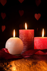 Three wax flame candlelight with ribbon in dark romantic light on hearts background, love dating, Valentine's day, selective focus