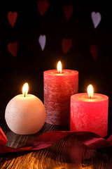 Fototapeta na wymiar Three wax flame candlelight with ribbon in dark romantic light on hearts background, love dating, Valentine's day, selective focus