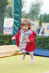 Fototapeta premium Little girl on playground in a park, jumping on trampoline Little Girl on a Trampoline.