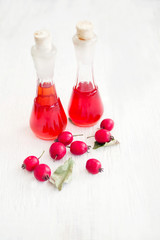 Hawthorn tincture in glass bottles and fresh hawthorn berries on a white wooden surface, soft focus