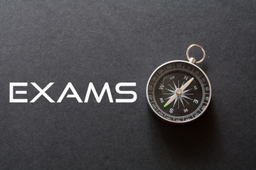 Exams word written on black background with compass