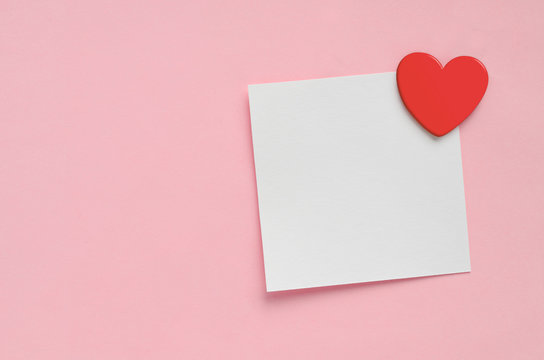 Blank paper note and red heart on pink paper background. Valentine's Day.