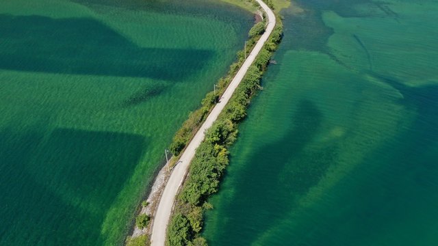 Aerial view of road over the Trebisnjica river, Lastva village, Bosnia and Herzegovina. Turquoise water, green bushes along the road. Minimalism.