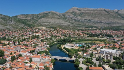 Aerial view of stone bridge (Kameni Most) on Trebisnjica river in Trebinje Old Town. Bosnia and Herzegovina. Summer sunny day, Turquoise water, mountains, trees, blue sky, small houses.