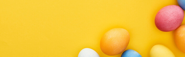 top view of multicolored painted Easter eggs on yellow background with copy space, panoramic shot