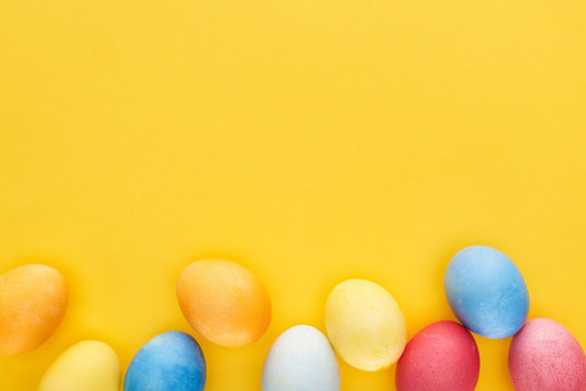 top view of multicolored painted Easter eggs on yellow background with copy space