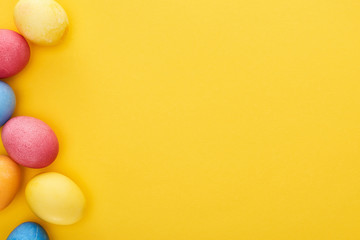 top view of multicolored painted Easter eggs on yellow background with copy space