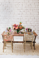 Served table for romantic dinner in style boho chic. Decor from fresh flowers peonies, roses, orchids and Leucospermum conocarpodendron. Crockery plates, glasses and candles. Wooden table and chairs.