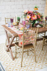 Served table for romantic dinner in style boho chic. Decor from fresh flowers peonies, roses, orchids and Leucospermum conocarpodendron. Crockery plates, glasses and candles. Wooden table and chairs.