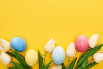 Top view of tulips and painted Easter eggs on colorful yellow background