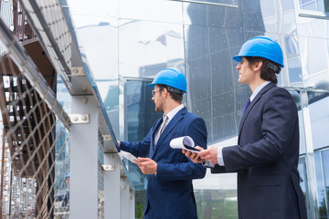 Real estate developers in helmets. New office construction. Confident business men and architect talking in front of modern office building.