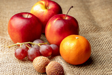 Three ripe red apples and other fruits on burlap.