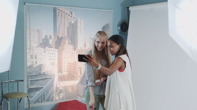 Backstage of the photo shoot: attractive black model making selfie with pretty make-up artist. They smiling and having fun.