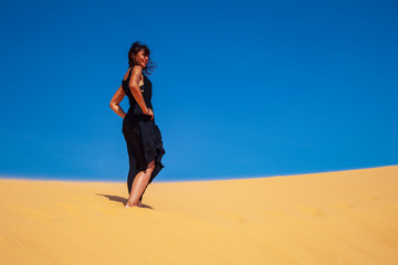 freedom concept, beautiful and happy girl jumping in the sand, in a black dress, joyful emotions