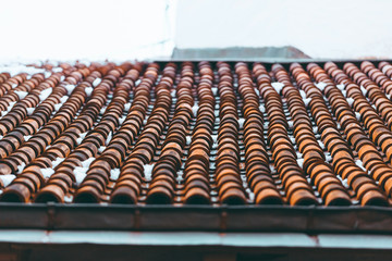 Tiled clay red roof in the snow. Medieval old roof in winter in European town. Clay tiles in a row. Tiled background. Building structure