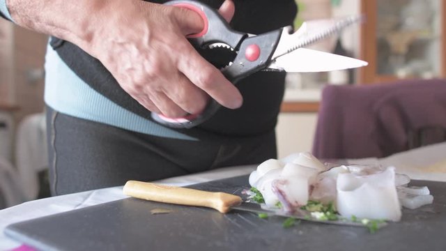 Unrecognizable people preparing squid indoor at home using scissors