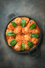 Meatballs in tomato sauce with bazil leaf in a frying pan on dark background. Top view. Copy space.