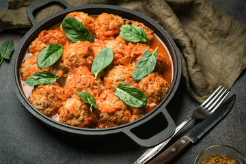 Meatballs in tomato sauce with bazil leaf in a frying pan on dark background. Top view.