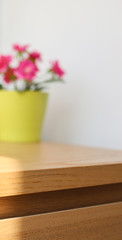 Defocused pink artificial flower in yellow flowerpot on wood closet drawer with white wall
