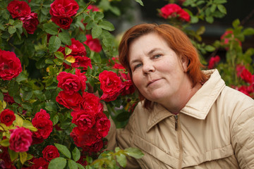 Elderly woman in the garden with roses. Gardener in the garden. Caring for flowers in the garden. Retired hobbies.