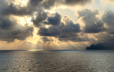 dramatic sea landscape, the sun in the sky behind the clouds over the dark sea