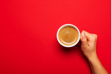 Female hand holding a white cup with black coffee on a red background.
