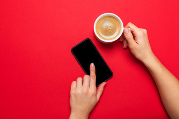 A Cup of coffee and a modern smartphone. black screen. red background.