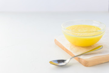 Melted butter (ghee) in a bowl on a wooden board. Horizontal orientation, copy space.