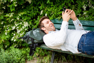 happy older man lying down on park bench looking at cellphone