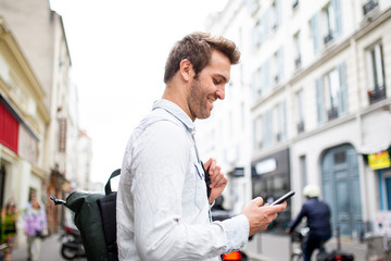 Side of middle age man smiling while looking at mobile phone in city