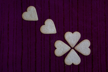 Heart-shaped cookies, four of them forming a four-leaf clover, isolated on dark red background.